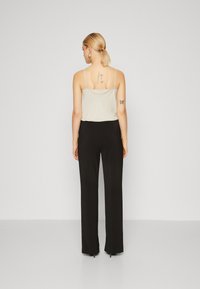 Black wide-leg pants paired with a light beige camisole. The camisole has thin straps and a relaxed fit. There are tattoos visible on the back.