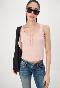 Pink ribbed crop top with lace trim, button detail, and thin shoulder straps, paired with light blue denim jeans and a black shoulder bag.
