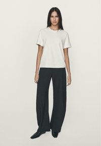 T-shirt bianco in cotone a maniche corte, abbinato a pantaloni neri a gamba larga. Tessuti lisci, design minimale, silhouette aderente.