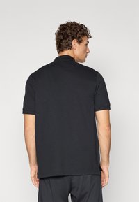 Sort polo shirt med klassisk krave, korte ærmer og sideslidser i kanten. Lavet af glat, let materiale.