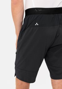 Bermudas negras para hombre hechas de un tejido ligero, que cuentan con una cinturilla suave, bolsillos laterales con cremallera y una textura perforada sutil.