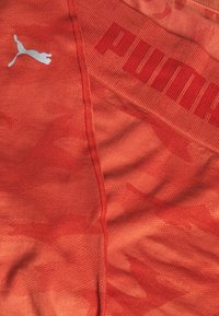 Czerwone spodenki sportowe z teksturowanym wzorem mają logo Puma w kolorze srebrnym. Pas jest prążkowany, a całość ma kontrastujące elementy wzornicze.