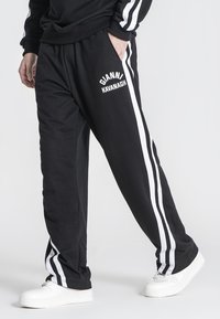 Sorte joggingbukser lavet af bomuld med hvide sidelommer. Har en elastisk talje og logoprint til venstre. Struktureret stof, afslappet pasform.