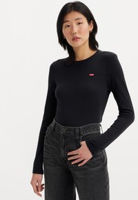 Body noir à manches longues avec une coupe ajustée, encolure ronde et un petit logo rouge Levi's sur la poitrine, associé à un jean taille haute gris.