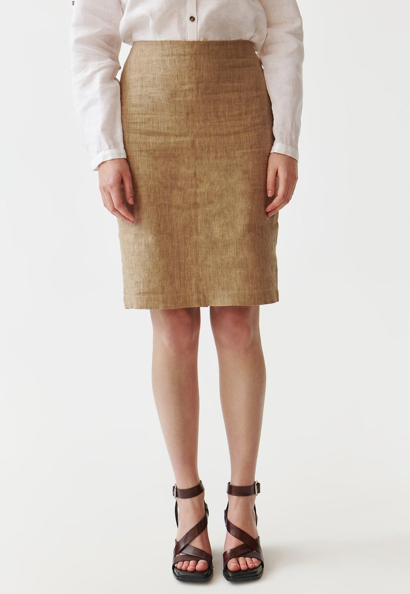 Une jupe ajustée, arrivant au genou, en tissu texturé beige, associée à des sandales brunes avec des courroies croisées et des boucles à la cheville.