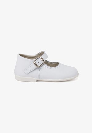 Białe dziecięce buty w stylu Mary Jane ze skóry, z falowanym brzegiem i paskiem na srebrną klamrę na białym tle.