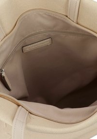 Beige draagtasje met een textuurstof aan de buitenkant. De binnenkant heeft een gladde voering, een ritsvak en een logo-label dat aan de binnenkant is gestikt.