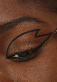 Svart eyeliner i lynform på en brun øyelokk. Jevn hudtekstur og mørke øyevipper som fremhever øyedetaljene.