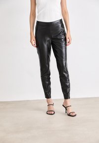Black leather pants with a slim fit, smooth texture, and a high waistband, paired with strappy black high-heeled sandals.