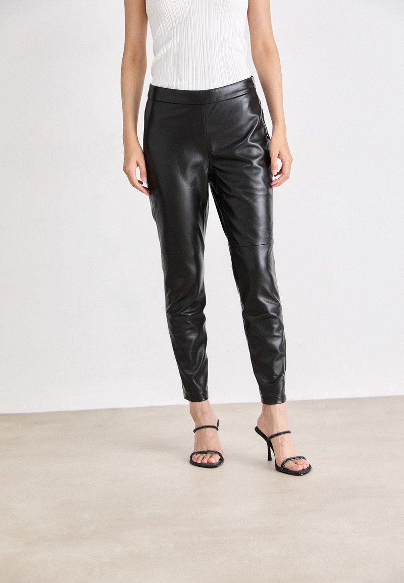 Black leather pants with a slim fit, smooth texture, and a high waistband, paired with strappy black high-heeled sandals.