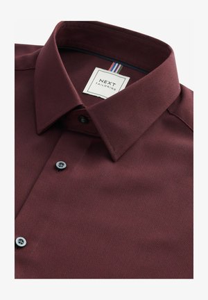 Burgunderfarbene Button-Down-Bluse aus strukturiertem Stoff, mit einem strukturierten Kragen, zwei schwarzen Knöpfen und einem Etikett mit bunten Streifen.