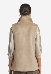 Beige faux fur ärmlös väst med hög krage, mjuk textur och avslappnad passform. Tyget ser lyxigt och varmt ut.