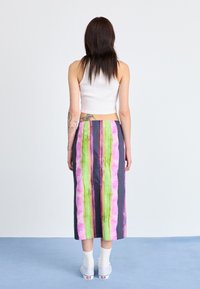 Mønstret, knelange skjørt med vertikale striper i rosa, grønn og lilla. Stoffet ser glatt ut, og har en glidelås i ryggen.