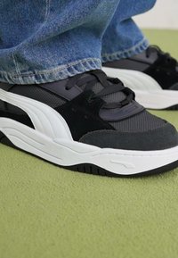Baskets noir et blanc avec un tissu texturé, des accents en daim et une semelle épaisse. Lacets gris et détail de logo sur le côté.