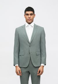 Gaišpelēks uzvalks ar izgrieztām piegāzēm un divām pogām, savienots ar balto svinīgo kreklu. Iezīmē augšmalu kabatas un taisnas piegriezuma bikses.