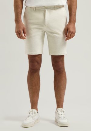 Lys beige shorts laget av teksturert stoff med en tettsittende midje, beltesløyfer og en ren kant. Kombinert med hvite sneakers.