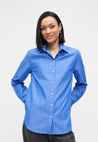 Blaues Hemd mit weißen vertikalen Streifen, mit Kragen, langen Ärmeln und abgerundetem Saum. Hergestellt aus einem glatten Stoff.