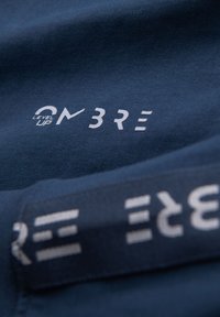 Detail z blízka navy modré látky s bílým textem "LEVEL UP ON 3RE" vytištěným na povrchu a opakovaným na přeložené části.