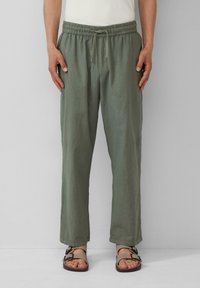 Pantalons légers, vert olive, avec une taille élastique, un cordon de serrage, des poches latérales et une coupe décontractée, associés à des sandales marron.