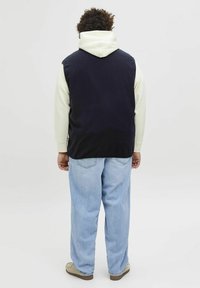 Granatowa kamizelka na lekki hoodie, luźne dżinsy i beżowe buty slip-on. Miękka faktura, casualowy design i luźny krój.