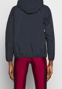 Marineblaue Windjacke mit Kapuze, elastischen Bündchen und Saum, die eine glatte Textur und ein leichtes Design aufweist.