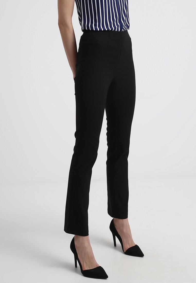 Femme portant un pantalon noir ajusté longueur cheville, des escarpins noirs pointus et un haut rayé vertical bleu et blanc.