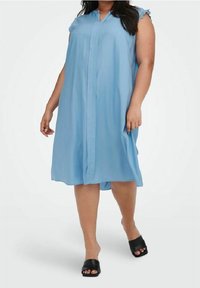 Světle modré šaty ke kolenům vyrobené z lehkého materiálu, s knoflíkovou légu, krátkými volánovými rukávy a volným střihem. Nosené s černými skládacími sandály.