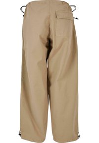 Pantalon beige à jambes larges avec ceinture élastique, poche arrière à rabat et cordons réglables à la taille et aux chevilles.