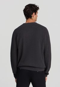 Maglione grigio scuro a maglia con finitura testurizzata, scollatura rotonda e polsini a costine. Design semplice e informale con una vestibilità rilassata.