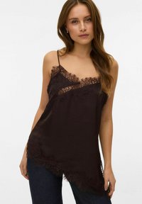 Czarny top na cienkich ramiączkach z koronkowym wykończeniem, lekko asymetrycznym dołem i delikatnymi, cienkimi ramiączkami. Gładka faktura z misternymi koronkowymi zdobieniami.