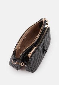 Sort quiltet læder crossover taske med guld lynlåse, åben hovedrum der viser beige mærket stofforing og en ydre lynlås lomme.