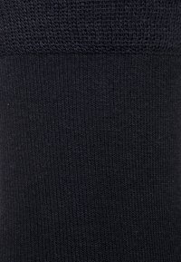 Schwarze kniehohe Socke aus geripptem Stoff. Verfügt über einen glatten oberen Rand und ein nahtloses Design, das Komfort und Elastizität bietet.