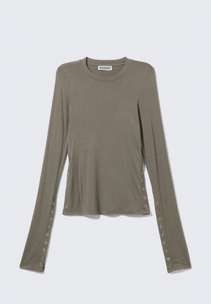 Haut à manches longues vert olive avec col rond, doté d'œillets métalliques le long des manches et des côtés, posé à plat sur un fond clair.