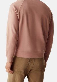 Světle růžová fleecová mikina s ribbovanými manžetami a lemem, s kulatým výstřihem a raglánovými rukávy, spárovaná s béžovými kalhotami.