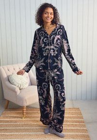 Tamsiai mėlynas florų rašto pižamų komplektas, turintis ilgomis rankovėmis, mygtukais užsegamą palaidinę ir kelnes su raišteliu, papuoštas rožinėmis detalėmis ir švelnia, lygi tekstūra.