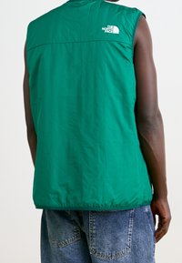 Chaleco sin mangas verde hecho de una tela suave, con un logo blanco en la parte trasera, con un diseño simple y aerodinámico sin cierres visibles.