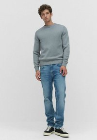 Lichtgrijze gebreide trui met ronde hals, gecombineerd met lichtblauwe jeans en zwarte sneakers. Textuurstof en geribde manchetten detail.