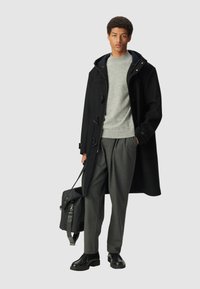 Cappotto duffle nero con chiusure a un pulsante, maglione grigio a maglia, pantaloni a righe e scarpe in pelle nere. Borsa nera con tracolla.