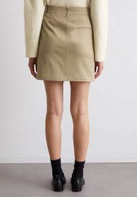 Jupe en denim kaki avec une coupe ajustée, dotée d'une poche arrière, de coutures visibles et d'un tissu légèrement texturé.