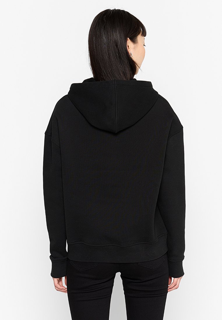 Zwarte hoodie met een ontspannen pasvorm, ribgebreide manchetten en zoom. Gemaakt van zacht materiaal met een gladde textuur.