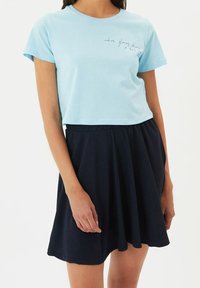 Camiseta de algodón azul claro con mangas cortas y cuello redondo, combinada con una falda skater azul marino de tejido texturizado.