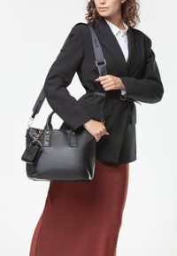 Bolso de cuero negro con herrajes dorados, asas dobles y una correa desmontable. Acompañado de un pequeño estuche de accesorios. Acabado texturizado.