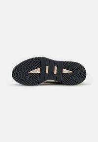 Podeszwa buta Adidas pokazująca czarną gumową powłokę z teksturowanymi i rowkowymi wzorami zapewniającymi przyczepność i elastyczność, na białym tle.