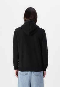 Hanorac negru din polar, cu buzunar tip kangur, manșete cu nervuri și glugă cu șnur, asortat cu pantaloni din denim de un albastru deschis.