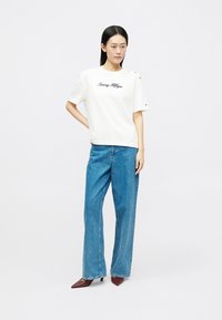 Λευκό κοντομάνικο μπλουζάκι με το "Tommy Hilfiger" κεντημένο σε μαύρο χρώμα, συνδυασμένο με μπλε φαρδιά τζιν παντελόνια και μπορντό ψηλές γόβες.