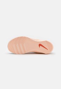 Nike urheilu kengän pohja vaalean persikan värissä, jossa on teksturoitu pintakuvio ja erottuva punainen swoosh-logo. Sileä pinta, jossa on selkeästi määritellyt urat.