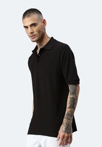 Polo nero con colletto, maniche corte e vestibilità comoda. Presenta una texture di tessuto liscia e una chiusura a tre bottoni.