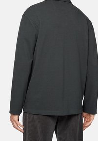 Tmavě šedá dlouhá košile s texturovanou tkaninou, s límečkem a rovný střihem, zobrazená zezadu.