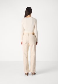 Maglioncino crema con design corto e polsini a coste, abbinato a pantaloni beige chiaro a vita alta. Tessuto liscio e dettagli minimi.