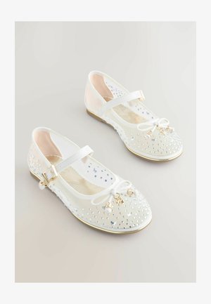 Weiße Ballerinas mit transparentem Mesh-Obermaterial, verziert mit silbernen Nieten, ausgestattet mit einer Schleife, goldenen Akzenten und einem Riemen mit Schnalle.